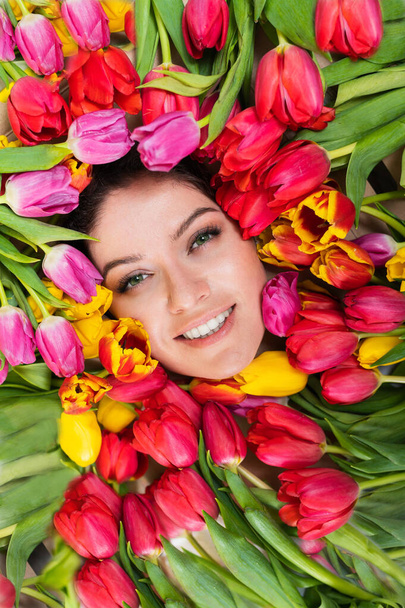 Portrait of a young beautiful woman with tulips around her face. The girl lies in the flowers given for March 8th. International Womens Day. - 写真・画像