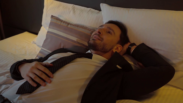 šťastný podnikatel v obleku odpočívá na posteli v hotelovém pokoji  - Záběry, video