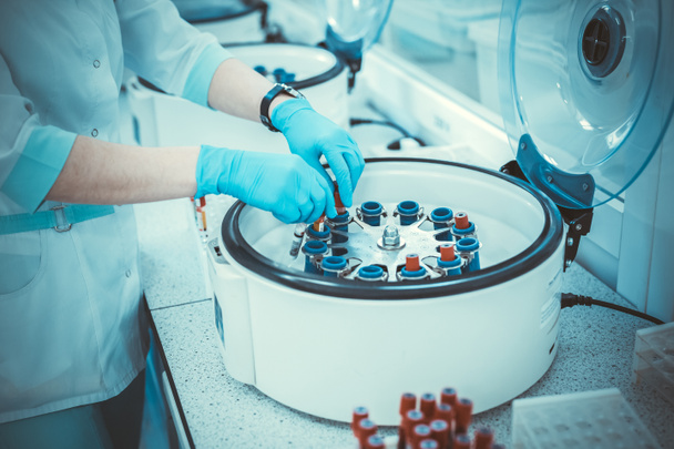 Nahaufnahme eines Forschers, der Hand in sterilen Handschuh das Reagenzglas in eine Laborzentrifuge steckt. Blutanalyse - Foto, Bild