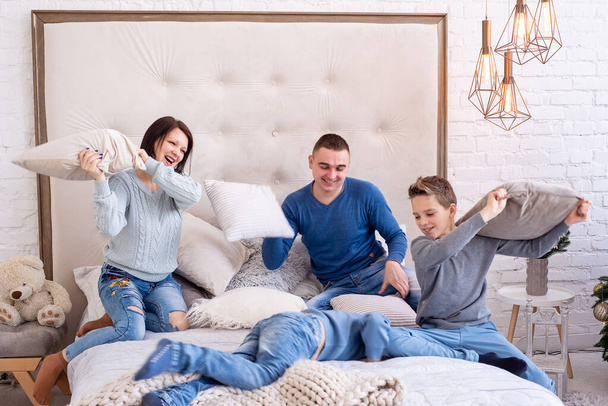 Glückliche Familie spielt in Kissenschlacht auf dem Bett zu Hause. Mutter, Vater und 2 Kinder liegen auf einem Bett. Zwei Söhne mit Eltern, die glücklich sind und Spaß zu Hause haben. Schöne Familie bleibt zu Hause. Quarantäne - Foto, Bild
