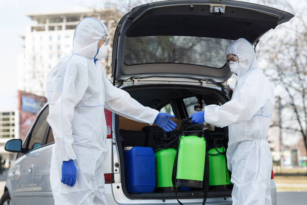 Pessoas em trajes protetores planejando fazer desinfecção com produtos químicos
 - Foto, Imagem