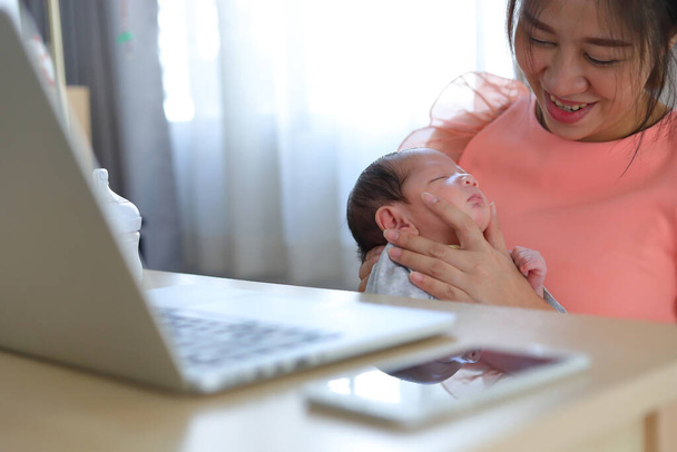 ビジネス・ホーム・オフィスで生まれたばかりの赤ちゃんを育てるビジネス・ウーマン母乳育児後に息子の腹を立てるのを手伝う母親 - 写真・画像