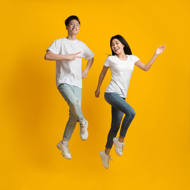 divertido asiático pareja felizmente saltar sobre amarillo fondo
 - Foto, imagen