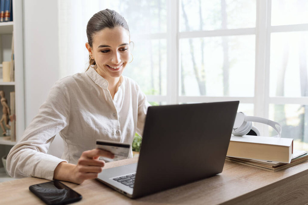 Smiling woman relaxing at home and doing online shopping on her laptop using a credit card - Photo, Image