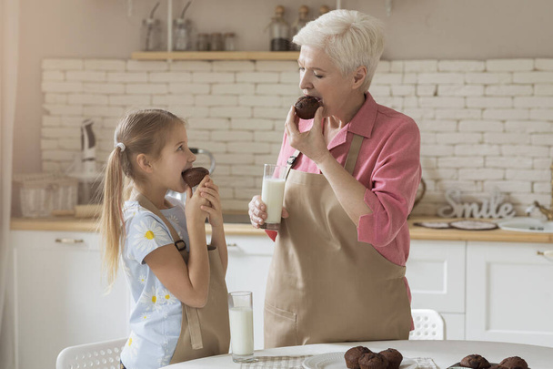 Yhdessä aika mummo ja hänen tyttärentyttärensä nauttia tuoreita muffineja keittiössä
 - Valokuva, kuva