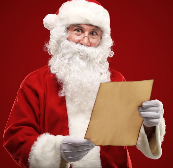 Portrait of happy Santa Claus holding Christmas letter and looking at camera - Foto, Imagen