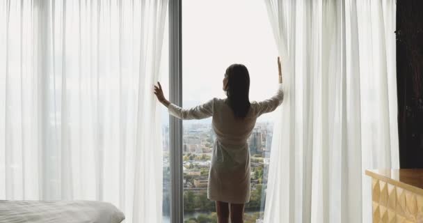 Rear view happy young brunette woman opening curtains. - Footage, Video