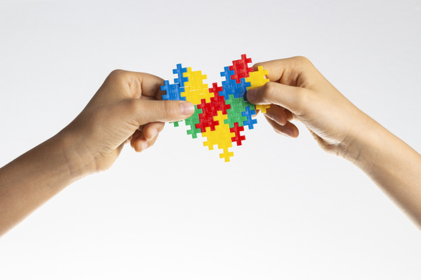 Światowy Dzień Świadomości Autyzmu. Dzieci ręce trzymając kolorowe serce puzzle na białym tle - Zdjęcie, obraz