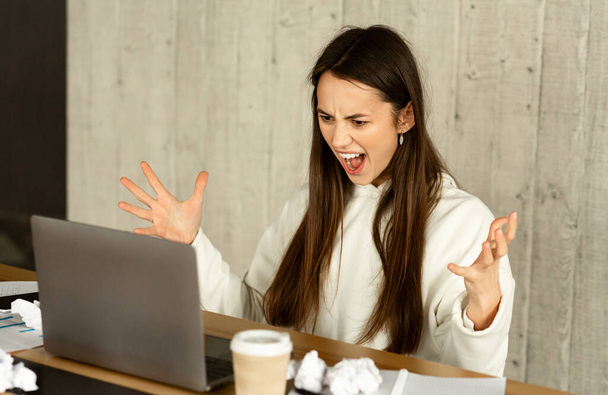 Αποτυχία στη δουλειά. Ανεξάρτητη κοπέλα φωνάζει στο φορητό υπολογιστή στο χώρο εργασίας - Φωτογραφία, εικόνα
