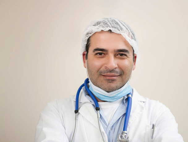 Kaukasischer Arzt lächelt mit Kopfbedeckung, Stethoskop und Gesichtsmaske. - Foto, Bild