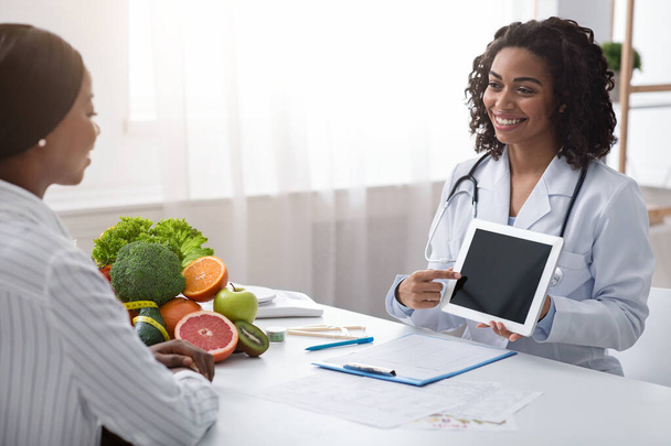 Nainen ravitsemusterapeutin avulla digitaalinen tabletti toimistossa, jolloin potilaat anamnesis
 - Valokuva, kuva