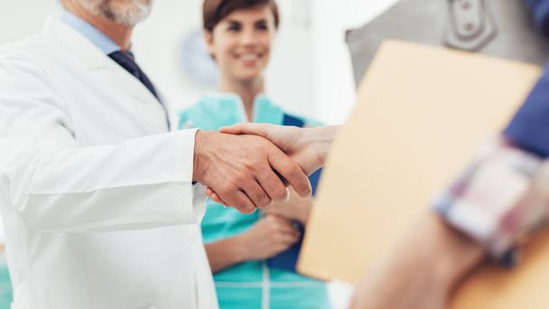 Medical staff welcoming a patient at the clinic: the doctor is giving an handshake and smiling, medical service and healthcare professionals concept, hands close up - Zdjęcie, obraz