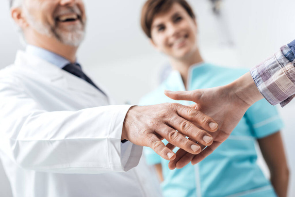 Medical staff welcoming a patient at the clinic: the doctor is giving an handshake and smiling, medical service and healthcare professionals concept, hands close up - Foto, imagen
