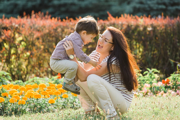 Mother having fun with cute son in summer park. Happy woman with cheerful little boy outdoors - Fotó, kép