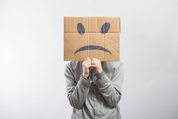 Молодой человек стоит с картонкой на голове с грустным лицом
 - Фото, изображение