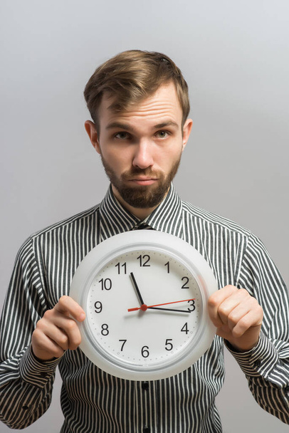 Portrait d'un jeune homme tenant une horloge avec ses mains sur fond gris
 - Photo, image