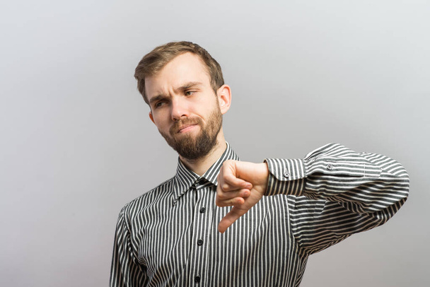 Portrait of confident young man in shirt and tie looking at camera and showing his thumbs down while standing against grey background - Фото, зображення
