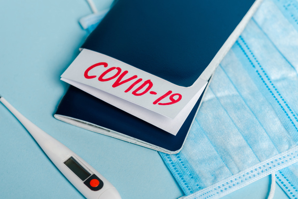 medische maskers, thermometer en paspoorten met covid-19 letters op blauwe achtergrond - Foto, afbeelding