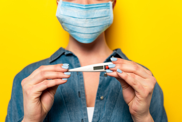 Selektiver Fokus der jungen Frau in medizinischer Maske mit Thermometer auf gelbem Hintergrund - Foto, Bild