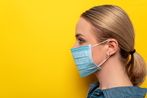 vista lateral de mujer joven en máscara médica sobre fondo amarillo, concepto coronavirus
 - Foto, Imagen