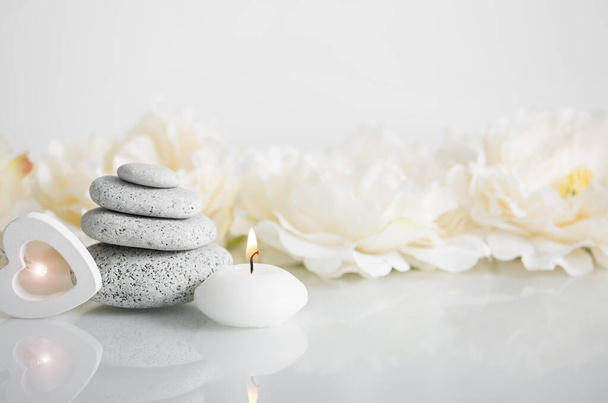 Stacked zen stones with white burning candle and blurred soft floral background, white glowing wooden heart light. Relaxing lifestyle concept. - Photo, Image
