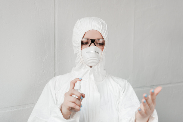 foco seletivo da pessoa em terno branco hazmat, respirador e óculos desinfetando as mãos com desinfetante de mão, conceito de coronavírus
 - Foto, Imagem