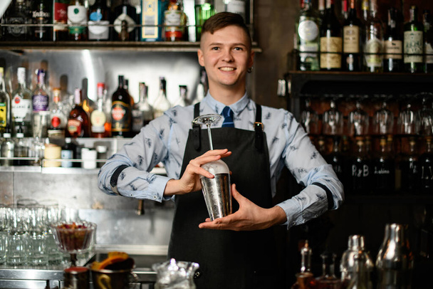 young smiling barman preparing glass and shaker to make cocktail. - Foto, immagini