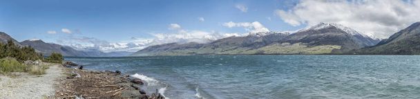 paisaje de lago alpino con playa y verdes costas de montañas cubiertas de nieve, disparado en la luz brillante de primavera de la playa del arroyo de la frontera, Otago, Isla del Sur, Nueva Zelanda
 - Foto, Imagen