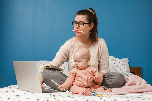 Mladá matka pracuje blízko dítěte v ložnici. Žena pracuje s laptopem.Práce z domova.  - Fotografie, Obrázek