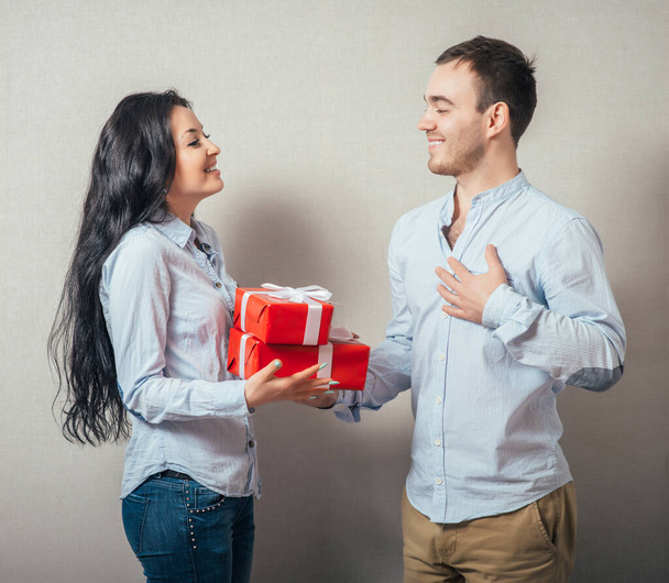 Girl is giving a gift to her boyfriend. Isolated on a gray background. - Foto, immagini