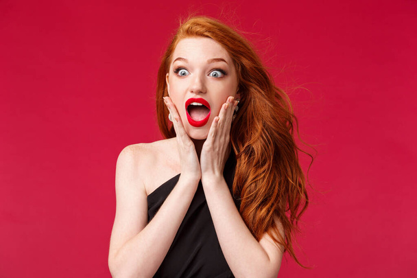 Makeup, beauty and women concept. Close-up portrait of astonished speechless redhead beautiful girl seeing something beautiful and awesome want to have it, losing speech, touch cheeks and drop jaw - Foto, Imagen