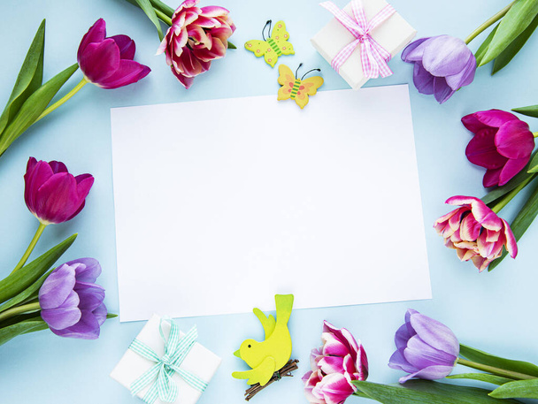 Üdvözlőlap. Tavaszi tulipán virágok és ajándék doboz pasztell kék háttér felülről lapos laikus stílusban. Köszöntés nőknek vagy anyáknak. - Fotó, kép