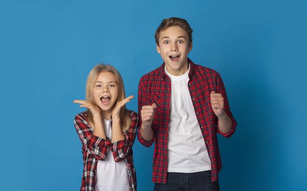 Hermano pequeño y hermana vitoreando con las manos levantadas sobre fondo azul
 - Foto, Imagen