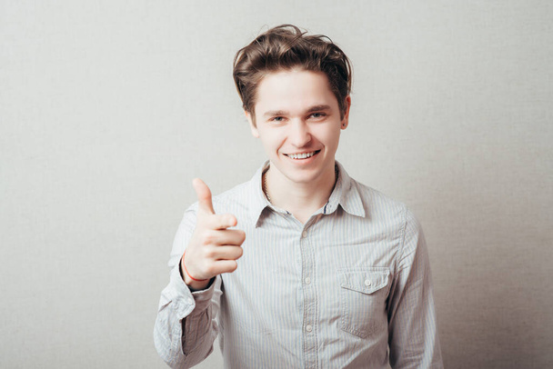 portrait of a young man pointing with his finger against a grey background - Фото, изображение