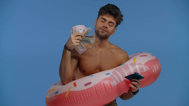 Shirtless man in swim ring holding money and passport isolated on blue - Felvétel, videó
