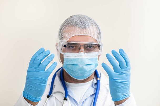 Kaukasischer Arzt mit Stethoskop, Schutzausrüstung und weißem Laborkittel isoliert auf weißem Hintergrund. - Foto, Bild