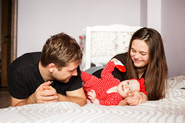 Les parents et un nouveau-né jouent à la maison. Des vêtements rouges. Rire et joie. Le concept de famille, d'amour, de garde d'enfants et de foyer
. - Photo, image