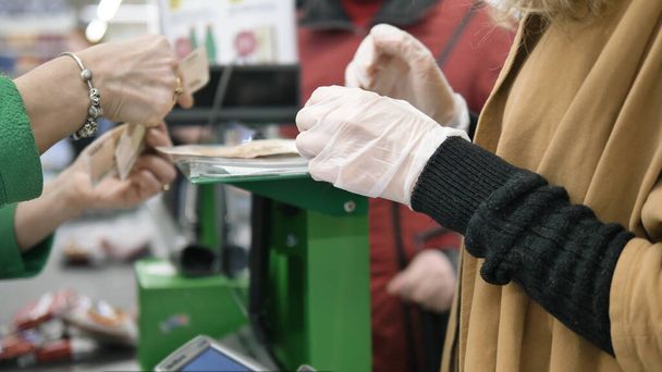 Žena na pokladně supermarketu vyzvedne drobné po nakupování v gumových ochranných rukavicích. Bezpečnostní opatření proti koronavirové infekci. - Fotografie, Obrázek