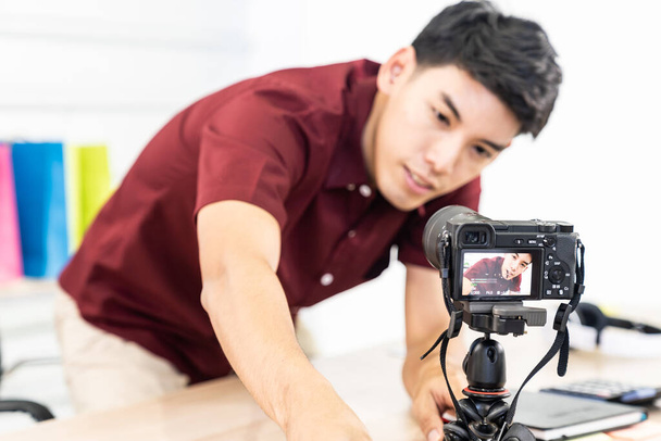 Young Asian male blogger setting up camera for recording live vlog video tutorial session at home. IT blogging or vlogging, social media hobby broadcasting, or online learning course concept. - Fotó, kép