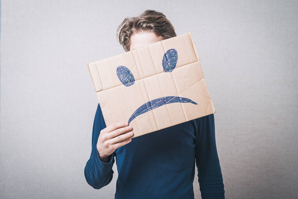 Young man with a cardboard on his head with sad face - Fotoğraf, Görsel