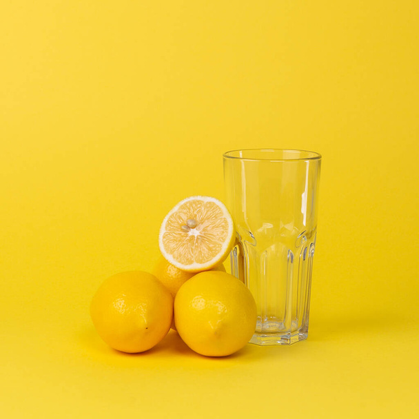 Limones y copa de vidrio vacía sobre un fondo amarillo
 - Foto, imagen