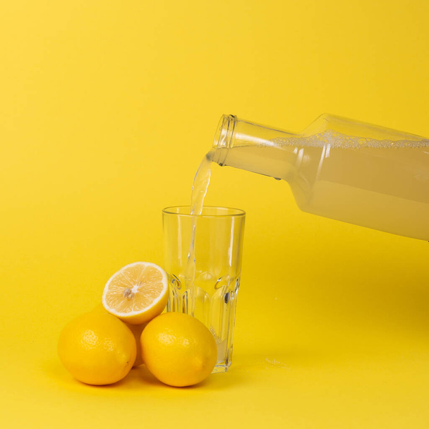 Lemon juice is poured into a glass with a glass bottle. Whole and cut lemons lie nearby. - Foto, afbeelding