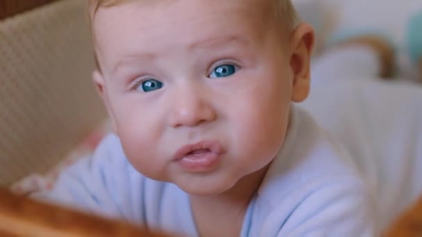 Csúszós portré édes újszülött kisfiúról, aki hason fekszik bölcsőjében és mosolyog, lassított felvételen - Felvétel, videó