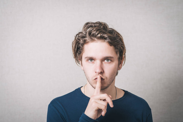Man shows his finger to his mouth quiet. Gray background. - Foto, Imagem