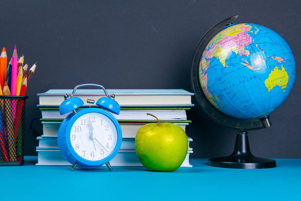 Una pila di libri con un globo, un bicchiere di matite, un orologio e mele
. - Foto, immagini