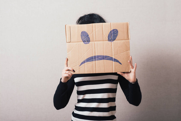 Vrouw bruin karton met een droevige glimlach. Grijze achtergrond - Foto, afbeelding
