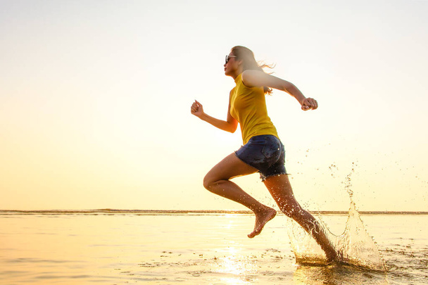 Femme pieds nus courant jogging dans les eaux peu profondes sur la plage au soleil du matin. Il y a des gouttes de gel d'arrêt de l'eau dans l'air avec le mouvement de la puissance. Pris avec la technique d'obturateur à grande vitesse
. - Photo, image