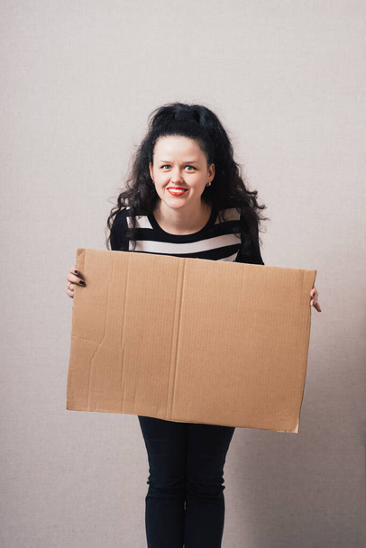 A woman holds a blank kraft paperboard. Gray background - Foto, Bild