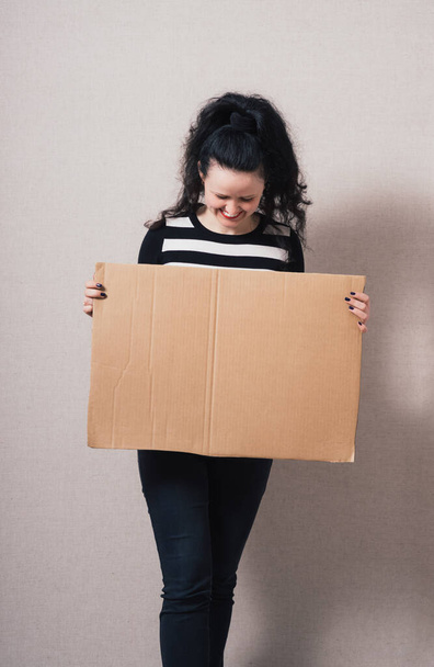 A woman holds a blank kraft paperboard. Gray background - Foto, Bild
