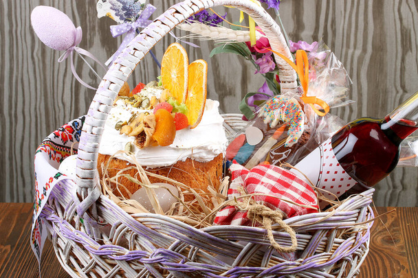 Decorative Easter basket with cake, colored eggs and liqueur. On a wooden table  - Фото, изображение